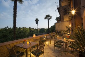 Un espacio exterior para comer con mesas y sillas, velas y vistas a palmeras y follaje.