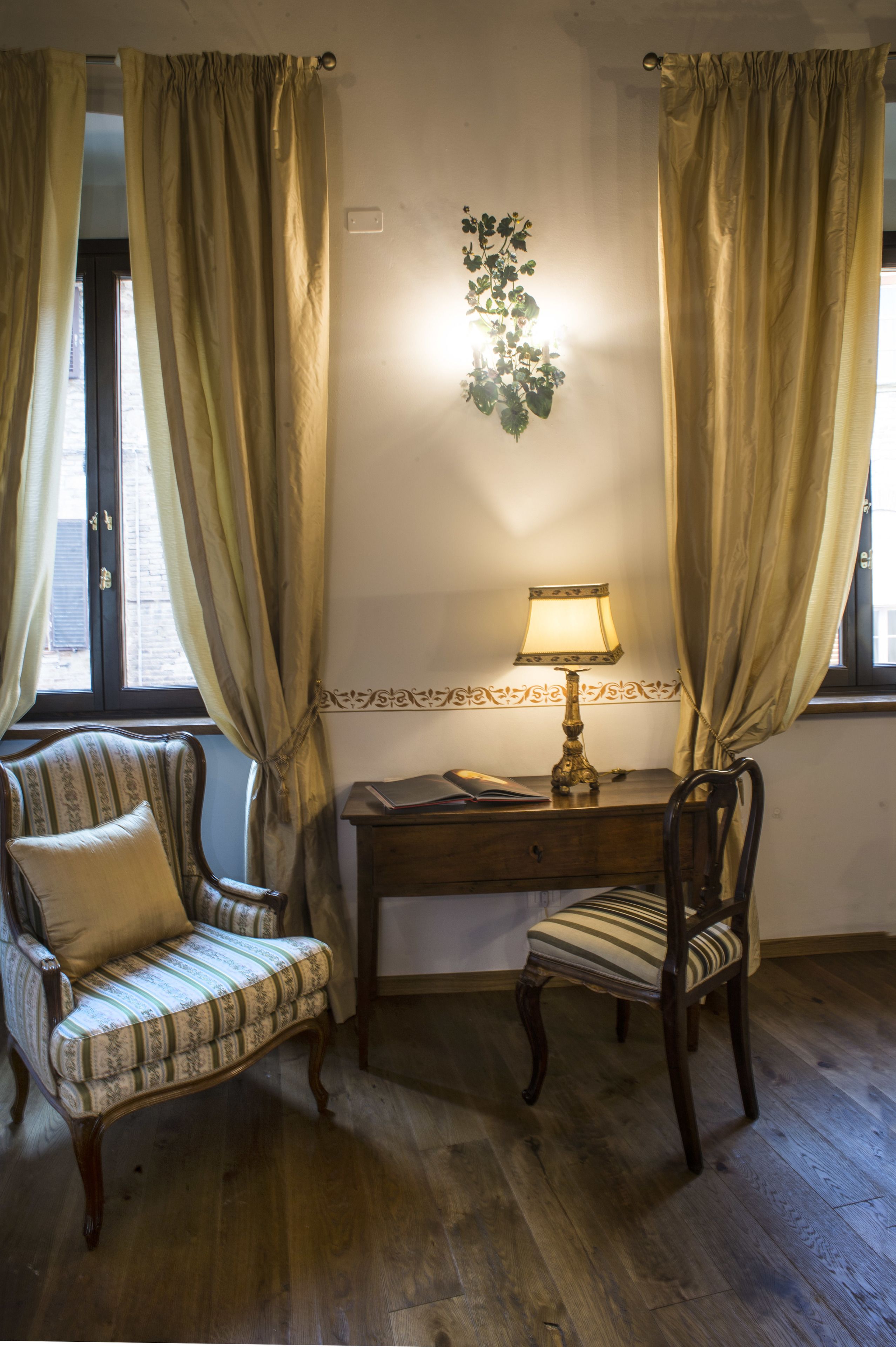 A room with a wooden desk, two chairs, a lamp, and curtains.