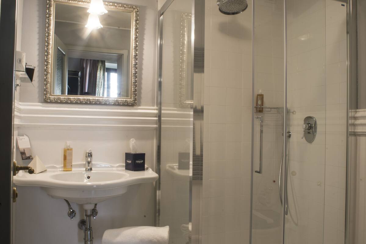 Un baño con ducha de vidrio, un lavamanos con espejo y suelo de baldosas.
