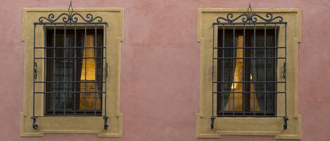 Due finestre con inferriate e cornici decorative su un muro rosa.
