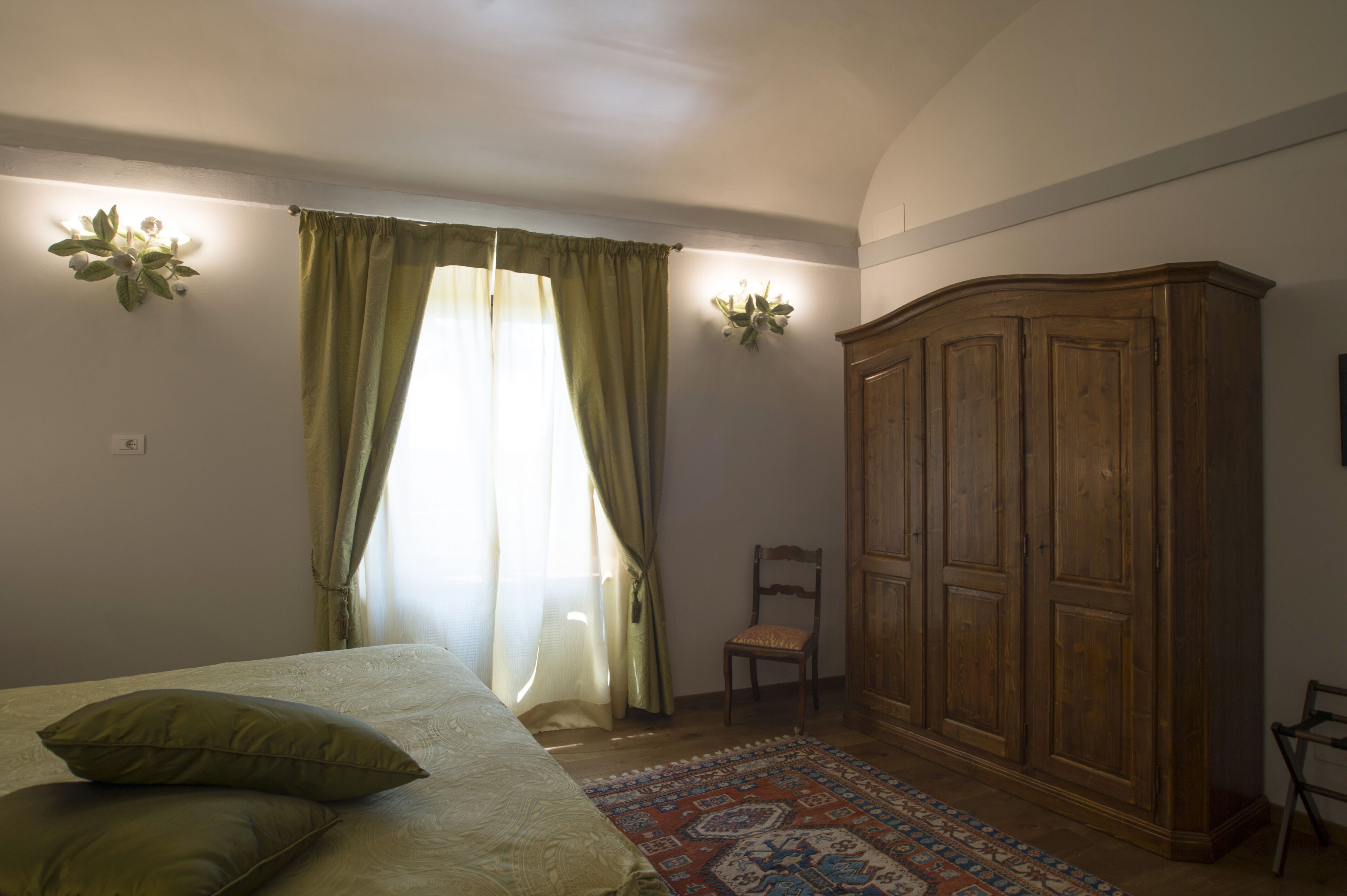 Ein Schlafzimmer mit einem Bett, einem Holzschrank, einem Sessel und einem gemusterten Teppich.