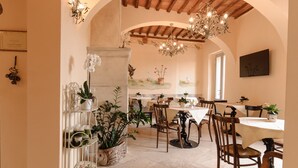 A dining area with wooden chairs and tables, a chandelier, and potted plants. - Palazzo Pacini (Colle di Val d'Elsa)