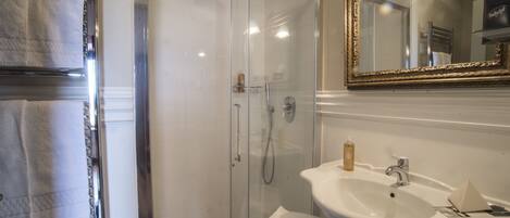 A bathroom with a glass-enclosed shower, a white sink with a mirror above it, and a towel rack with white towels.