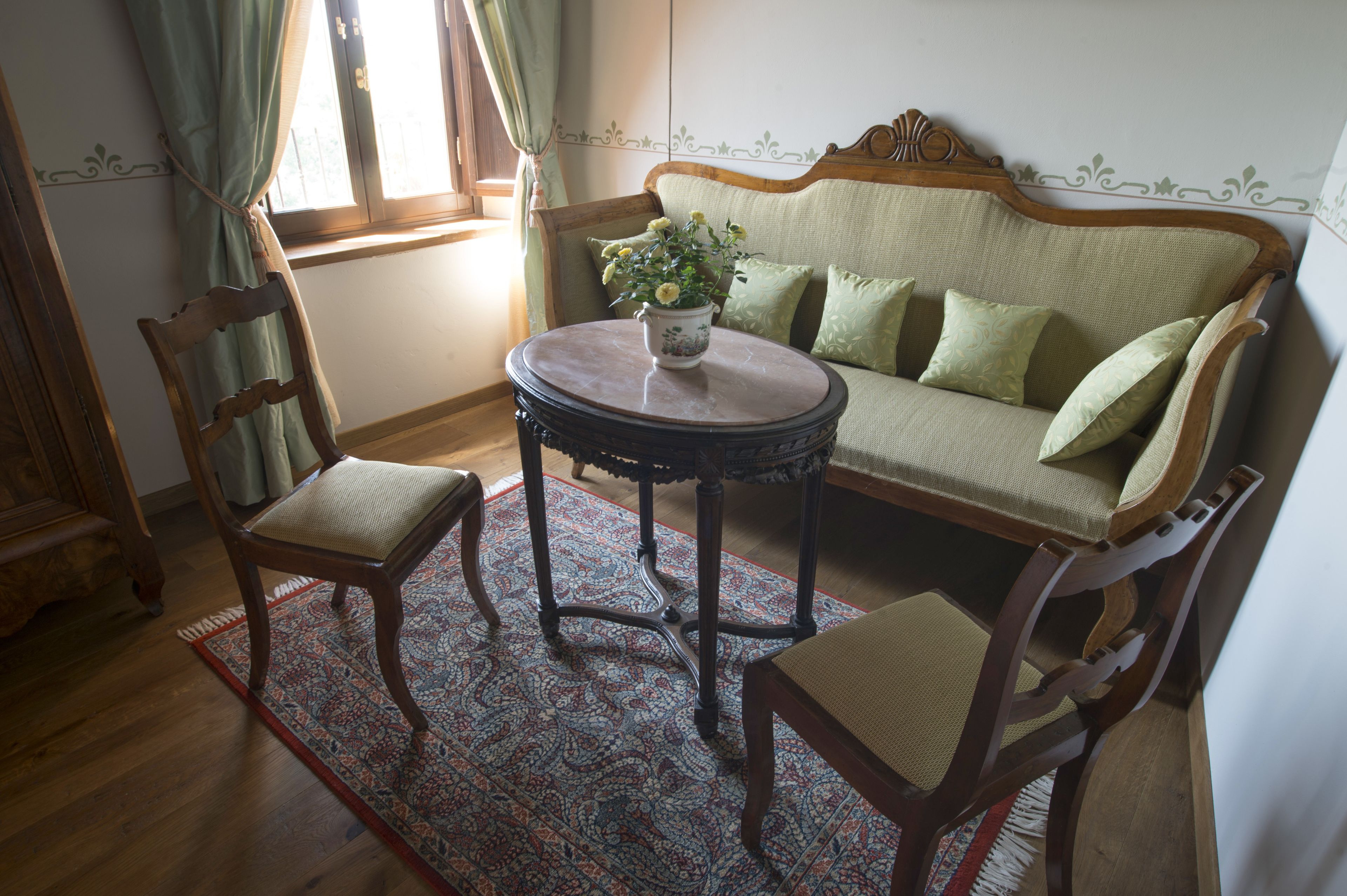 Ein traditionell eingerichteter Raum mit einer Holzsofa, zwei Stühlen, einem runden Tisch und einem gemusterten Teppich.