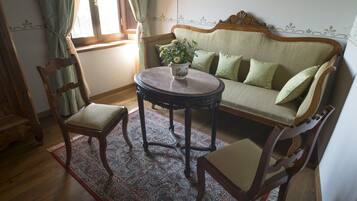 A traditional room with a wooden sofa, two chairs, a round table, and a patterned rug.