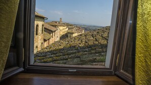 A view through a window of a stone staircase leading to a building with arched windows and a tower, overlooking a hilly landscape. - Palazzo Pacini (Colle di Val d'Elsa)