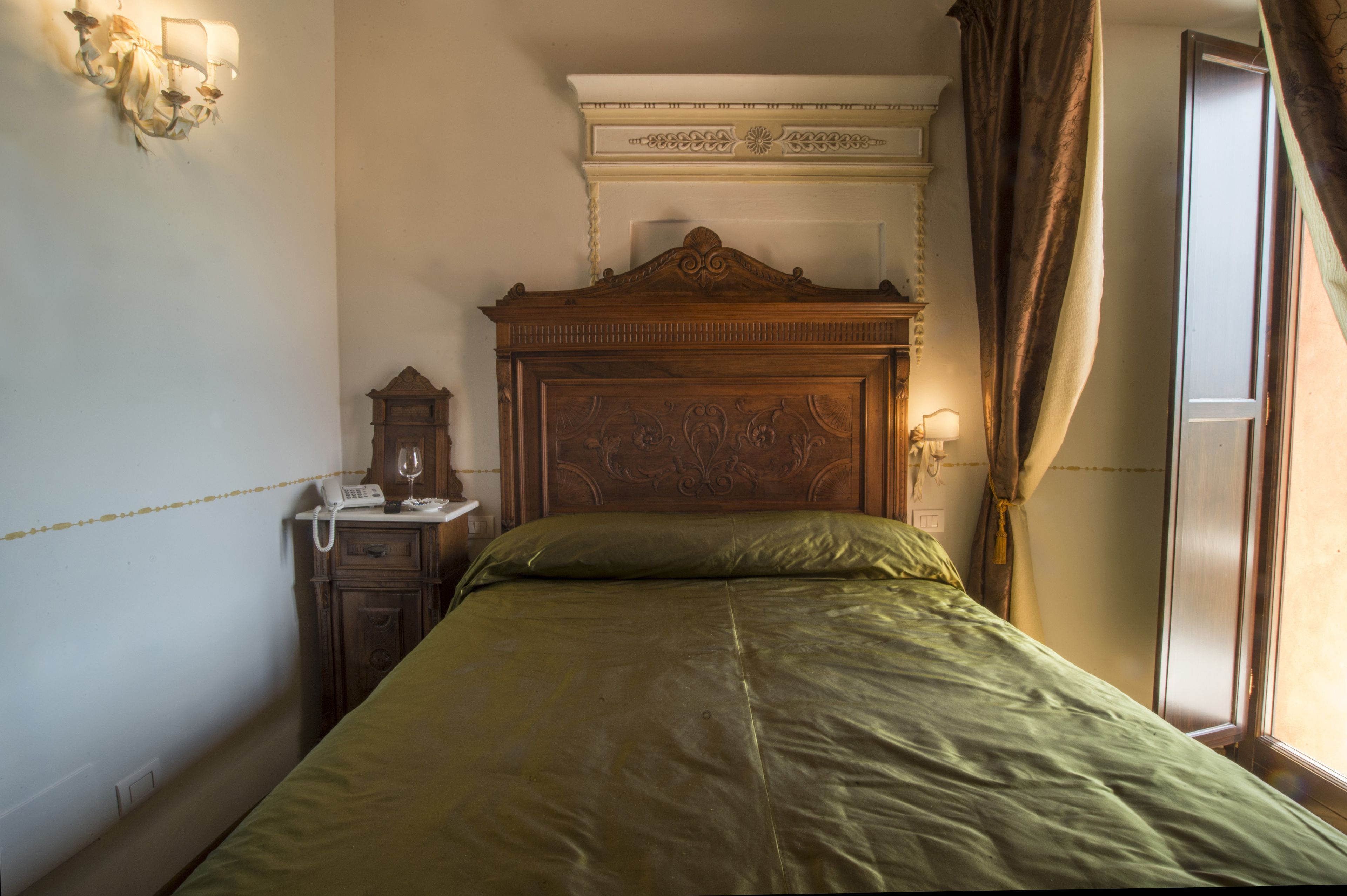 A bedroom with a wooden headboard, a green bedspread, a bedside telephone, and a wall-mounted light fixture.