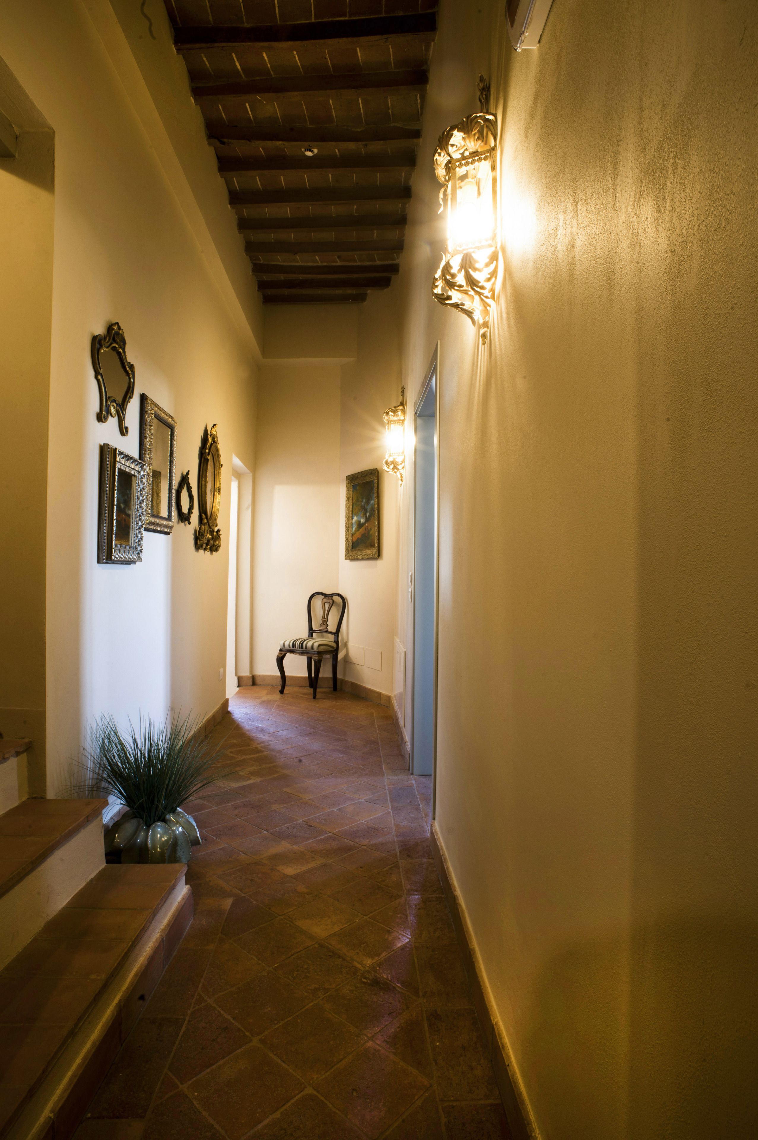 A hallway with a chair, decorative wall sconces, and a staircase.