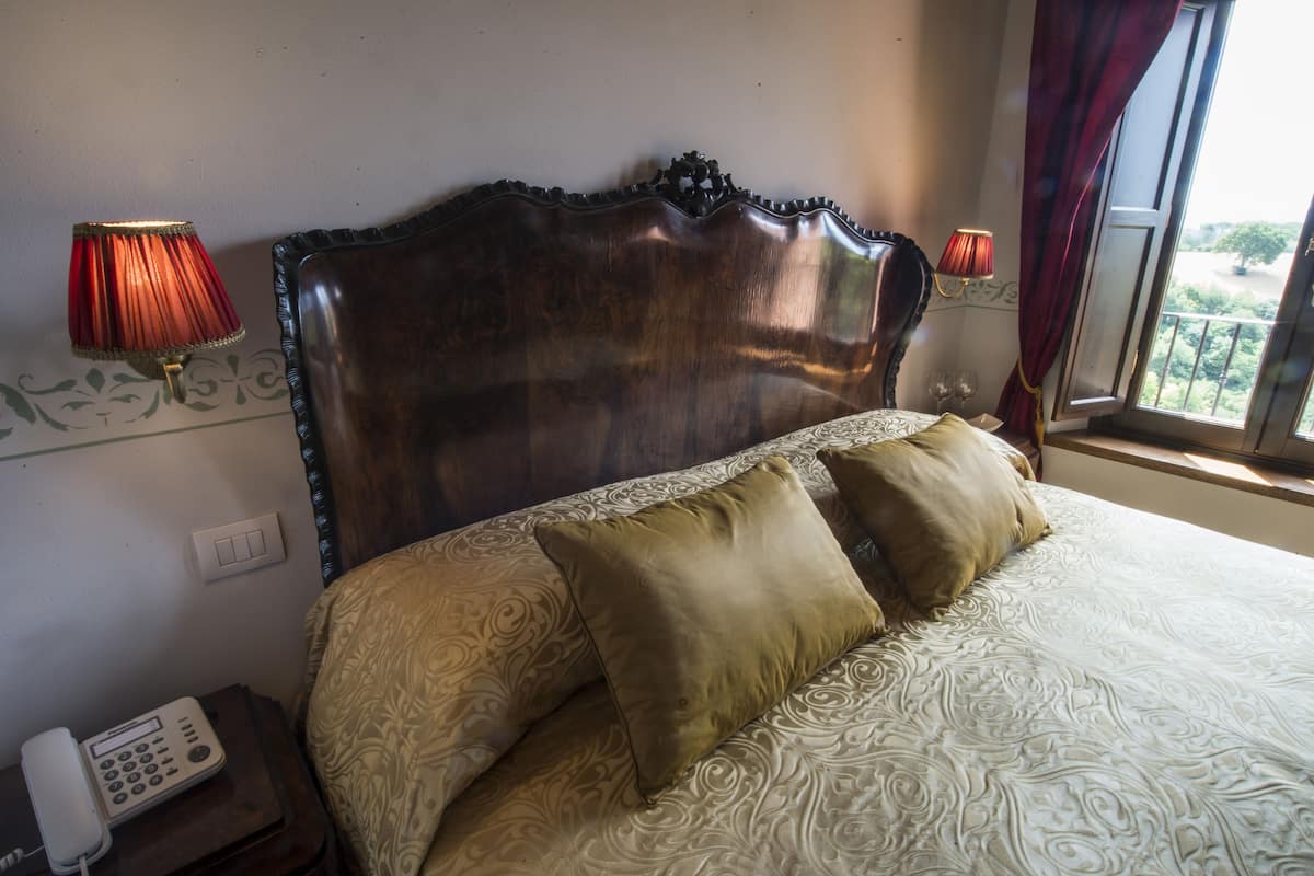 Una cama con cabecera de madera, dos lámparas, un teléfono y una ventana con cortinas.