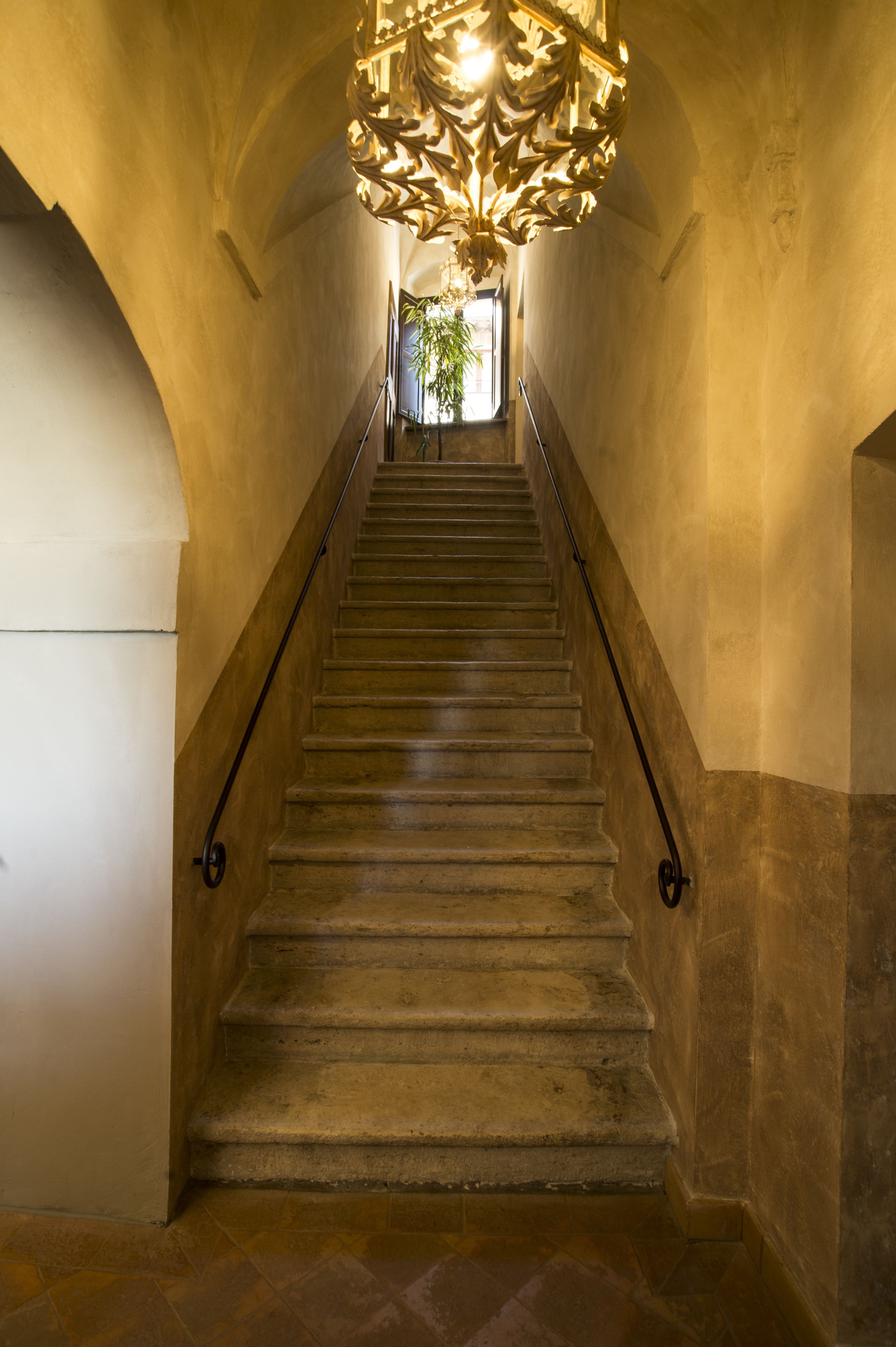 A grand staircase with ornate metal railings and a decorative ceiling light fixture.