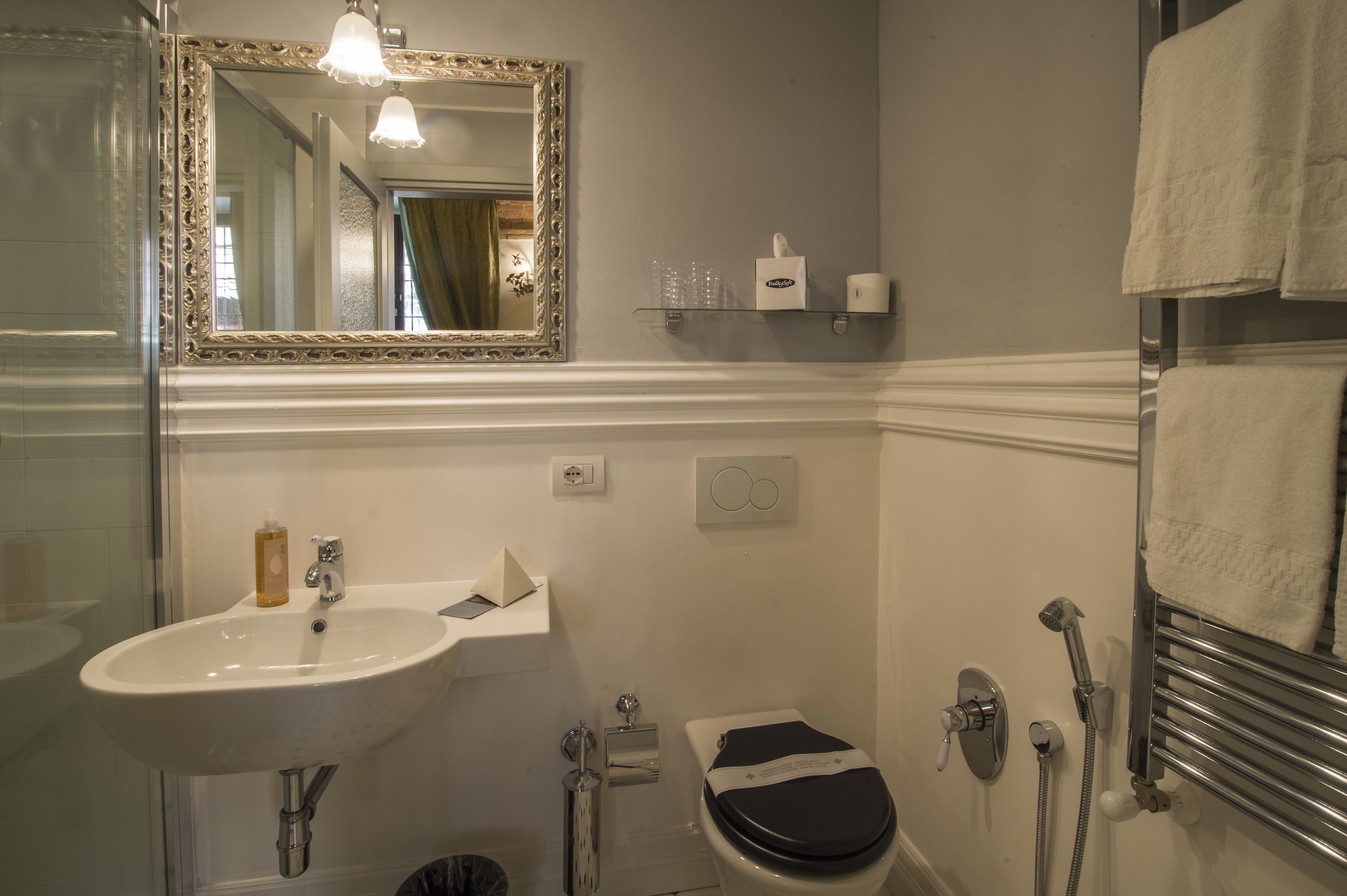 A bathroom with a white sink, a mirror with an ornate frame, a toilet, and a towel rack.