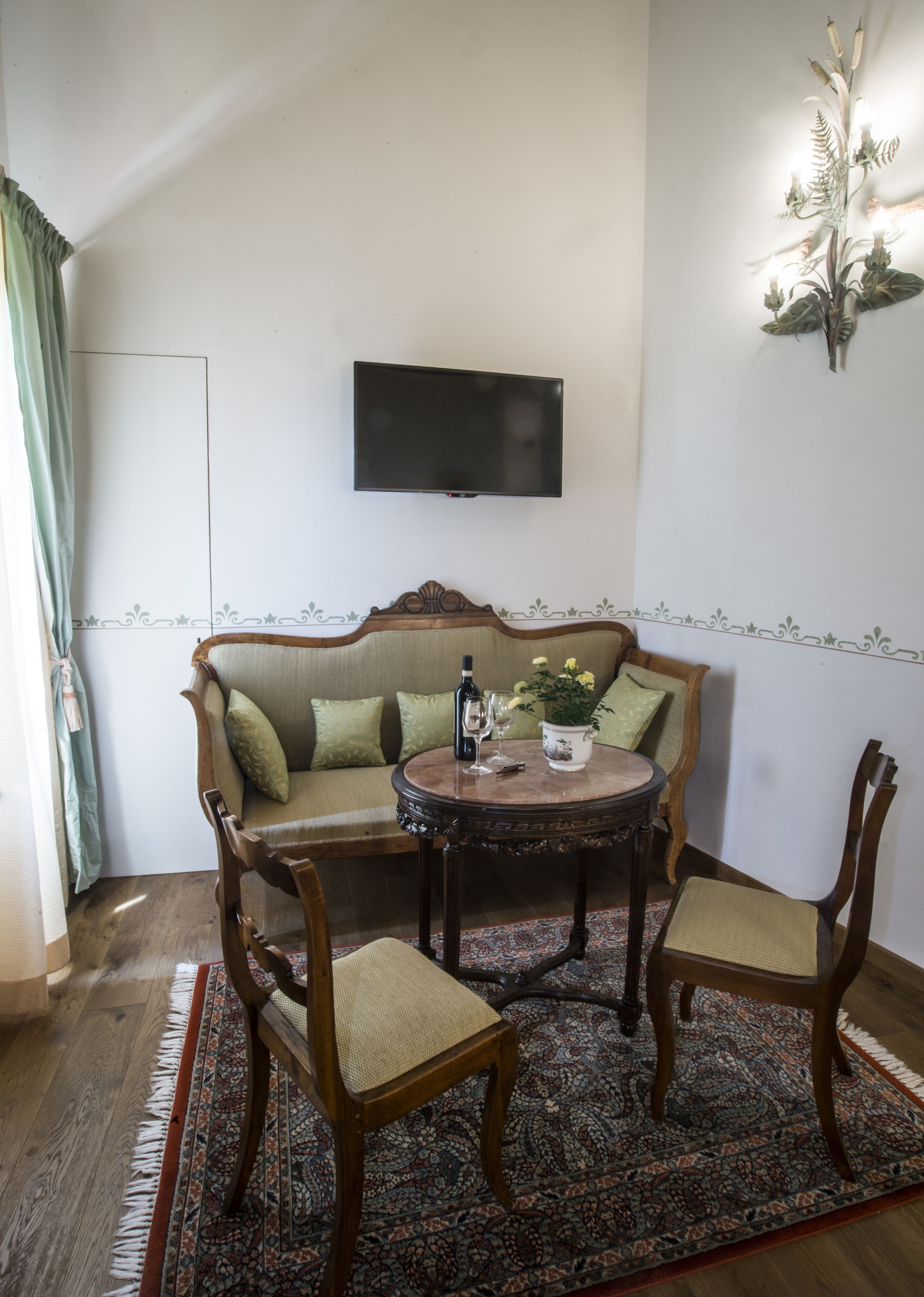 Un salón con sofá, dos sillones, una mesa redonda, un televisor montado en la pared y un adorno decorativo en la pared.