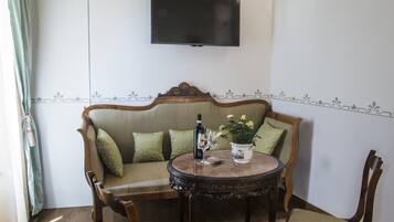 Un salon comprenant un canapé, deux fauteuils, une table ronde, un téléviseur fixé au mur et un élément décoratif mural.