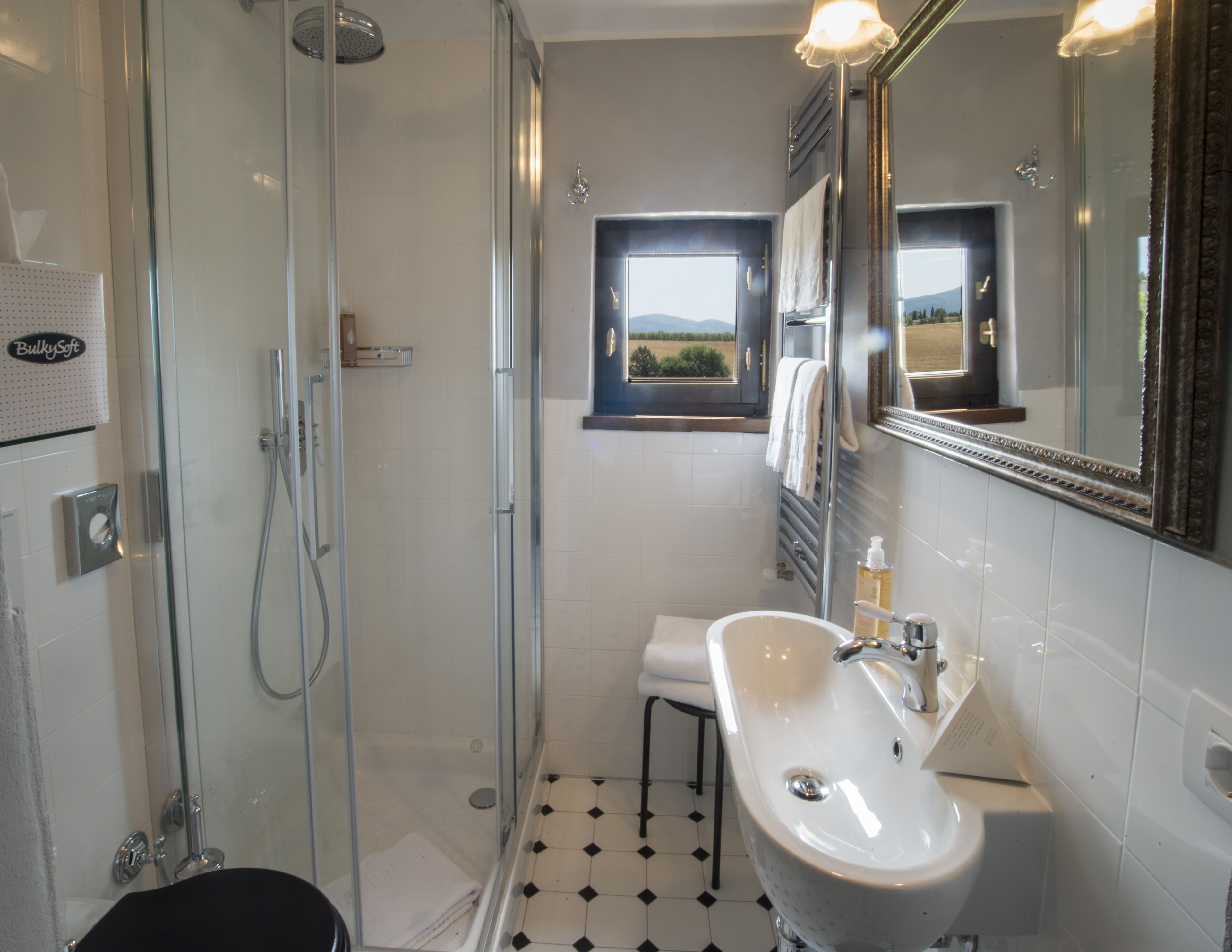 Un baño con ducha de mampara de vidrio, un lavabo con espejo y vistas al exterior a través de una ventana.