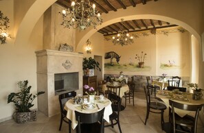 A dining area with multiple tables set for meals, a fireplace, and decorative wall art. - Palazzo Pacini (Colle di Val d'Elsa)