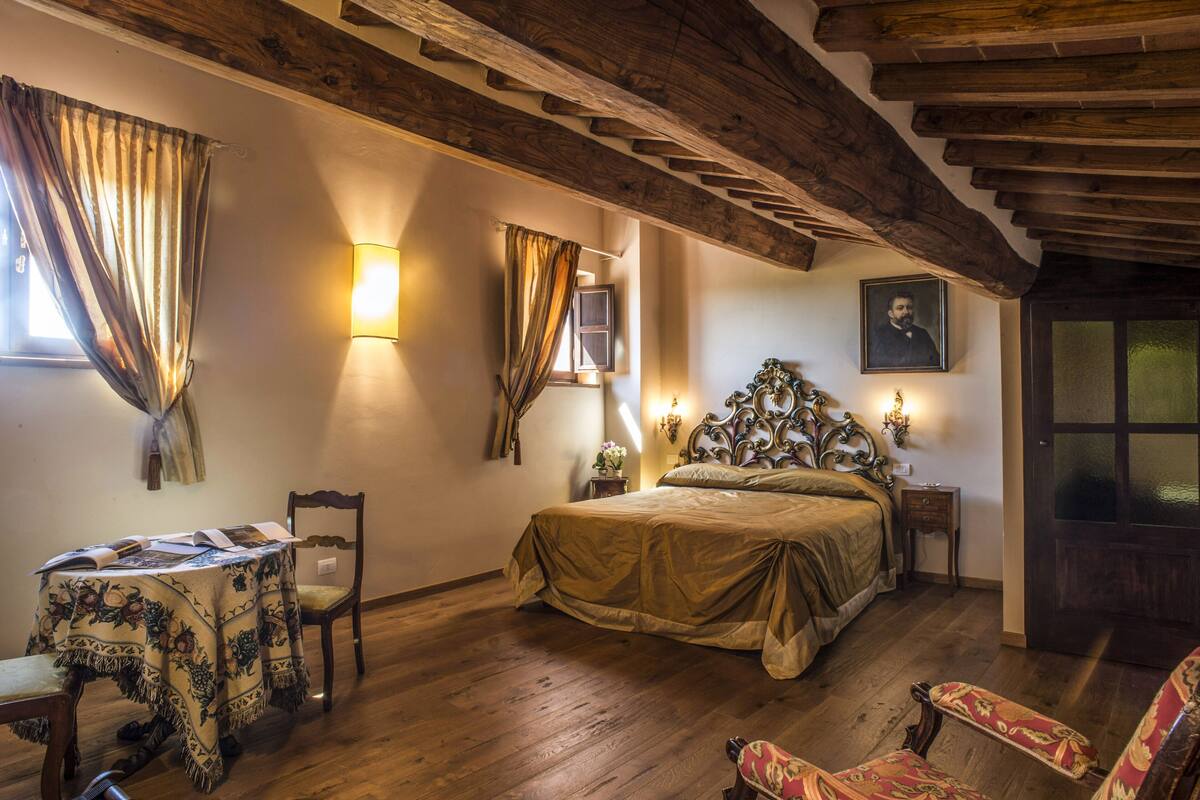Una habitación con techo de madera, una cama con cabecera, una mesa con mantel y una silla.
