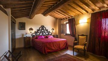 Una camera da letto con soffitto in legno, un letto con copripiumino rosso, una sedia, un comodino con una lampada e una finestra con tende.