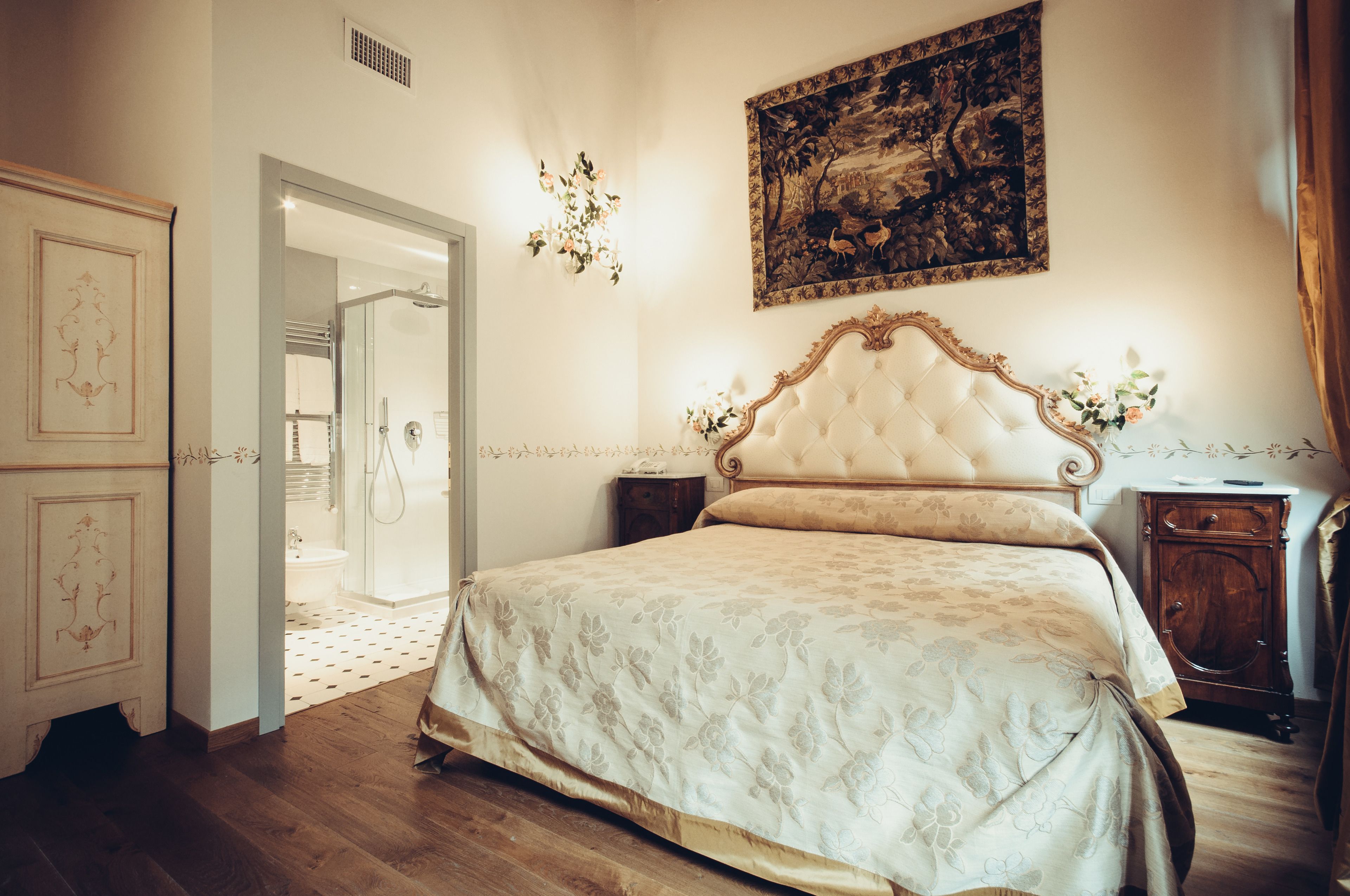 Een slaapkamer met een groot bed, een houten garderobe, een nachtkastje en een schilderij aan de muur.