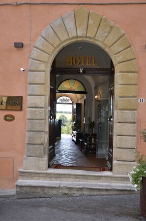 En hotelindgang med en buet stengang, et skilt med ordene "HOTEL" og udsigt til indretningen gennem glasdørene.