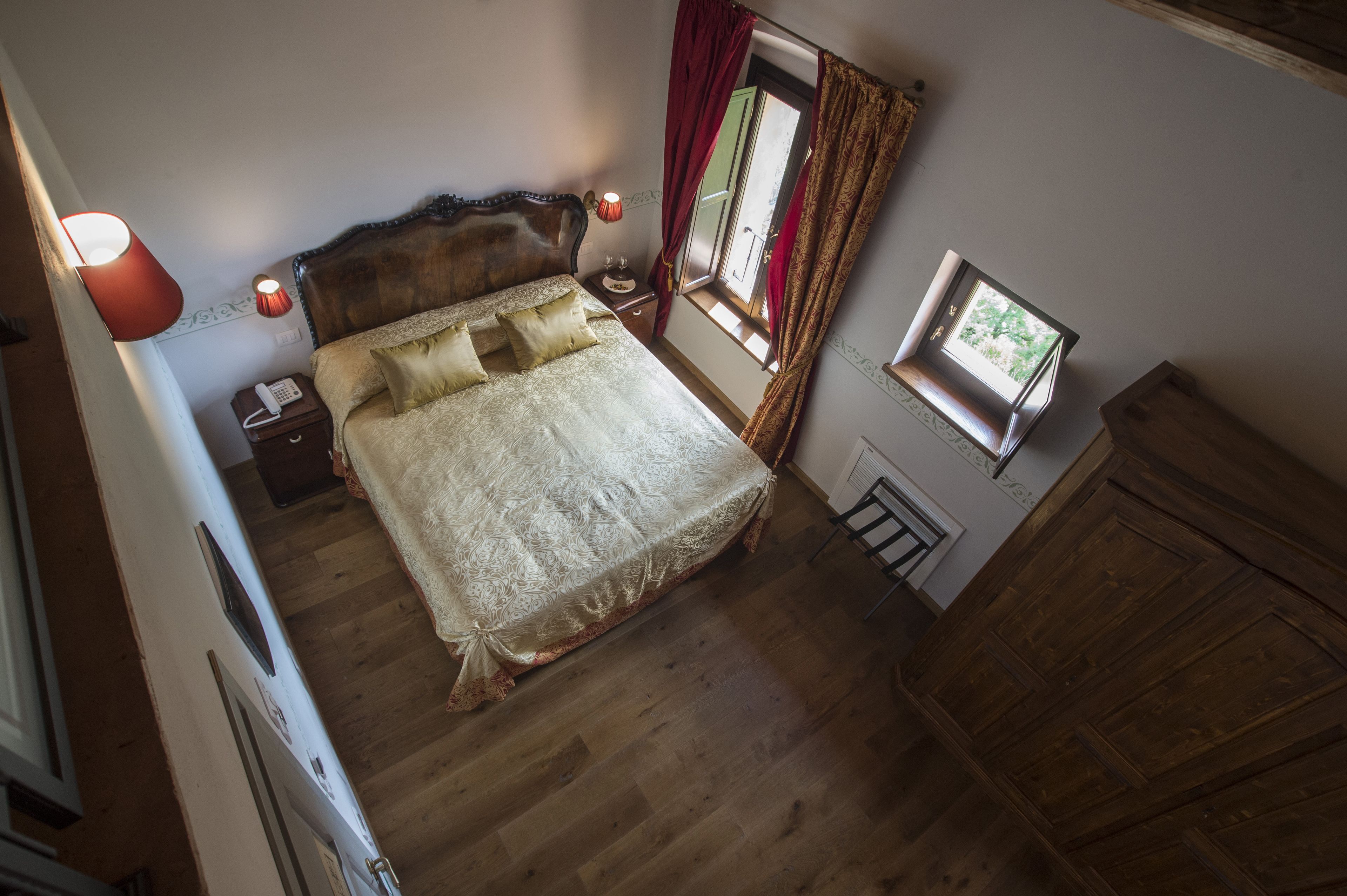Un dormitorio con una cama grande, lámparas de noche, una mesita de noche, una ventana con cortinas y un armario de madera.