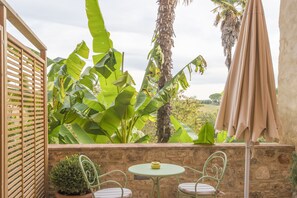 En terrasse med en stenvæg, to metalstole, et lille bord og en beige parasol.