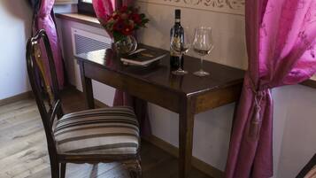 A dining area with a wooden table, a chair, and a sofa. There is a window with pink curtains, a vase with flowers, and two wine glasses on the table.