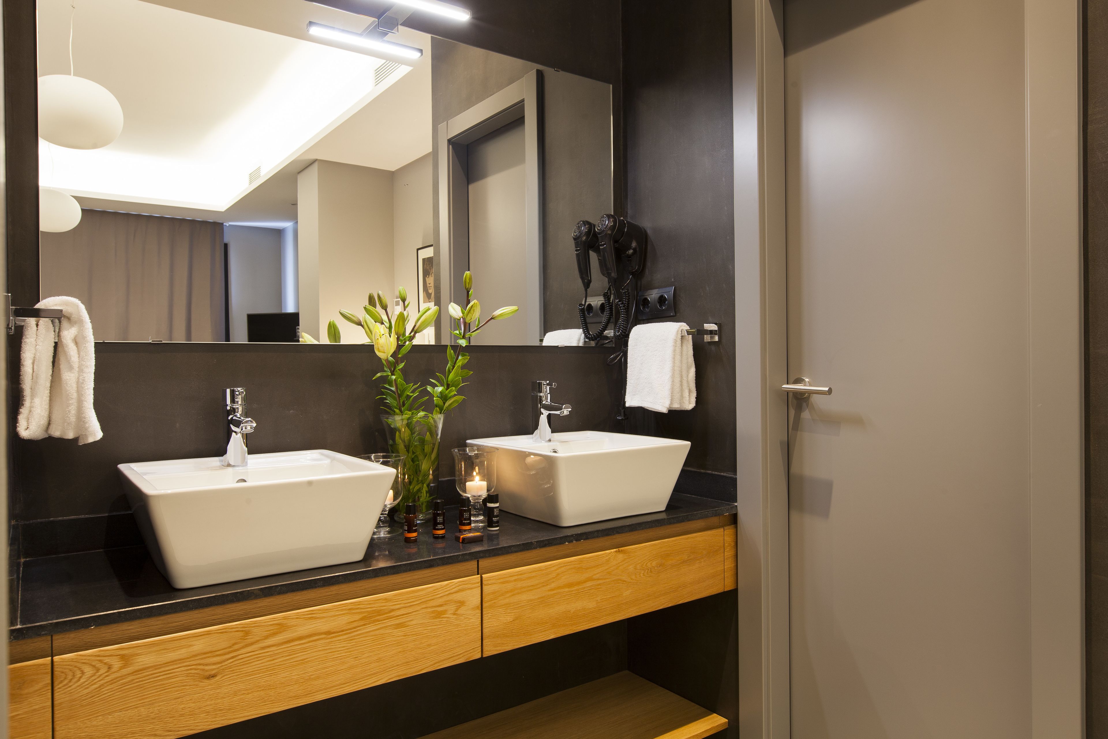 Uma casa de banho moderna com duas pias, um espelho grande e um secador de cabelo fixado na parede.