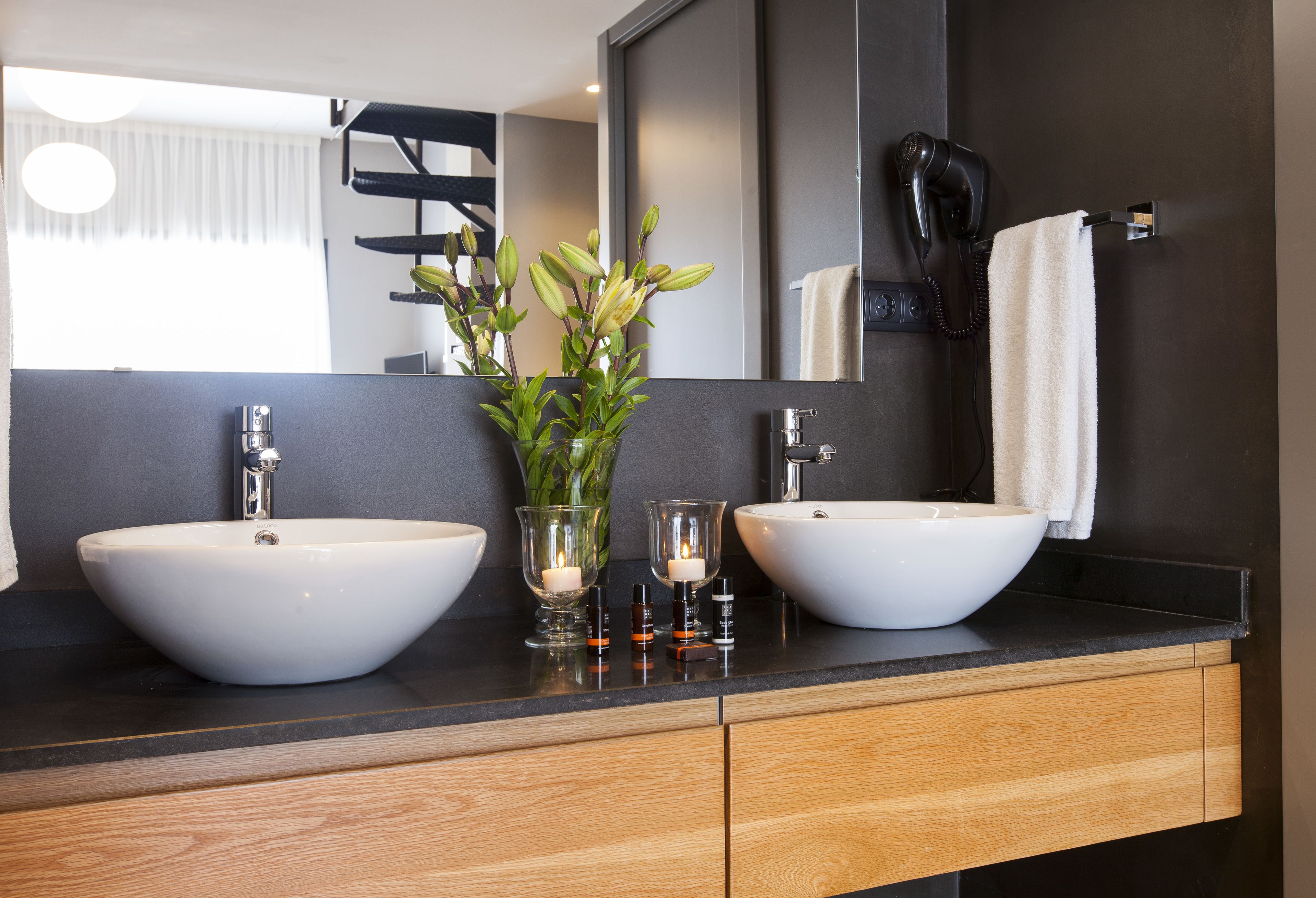 A modern bathroom with two white sinks, a mirror, and a hairdryer on the wall.