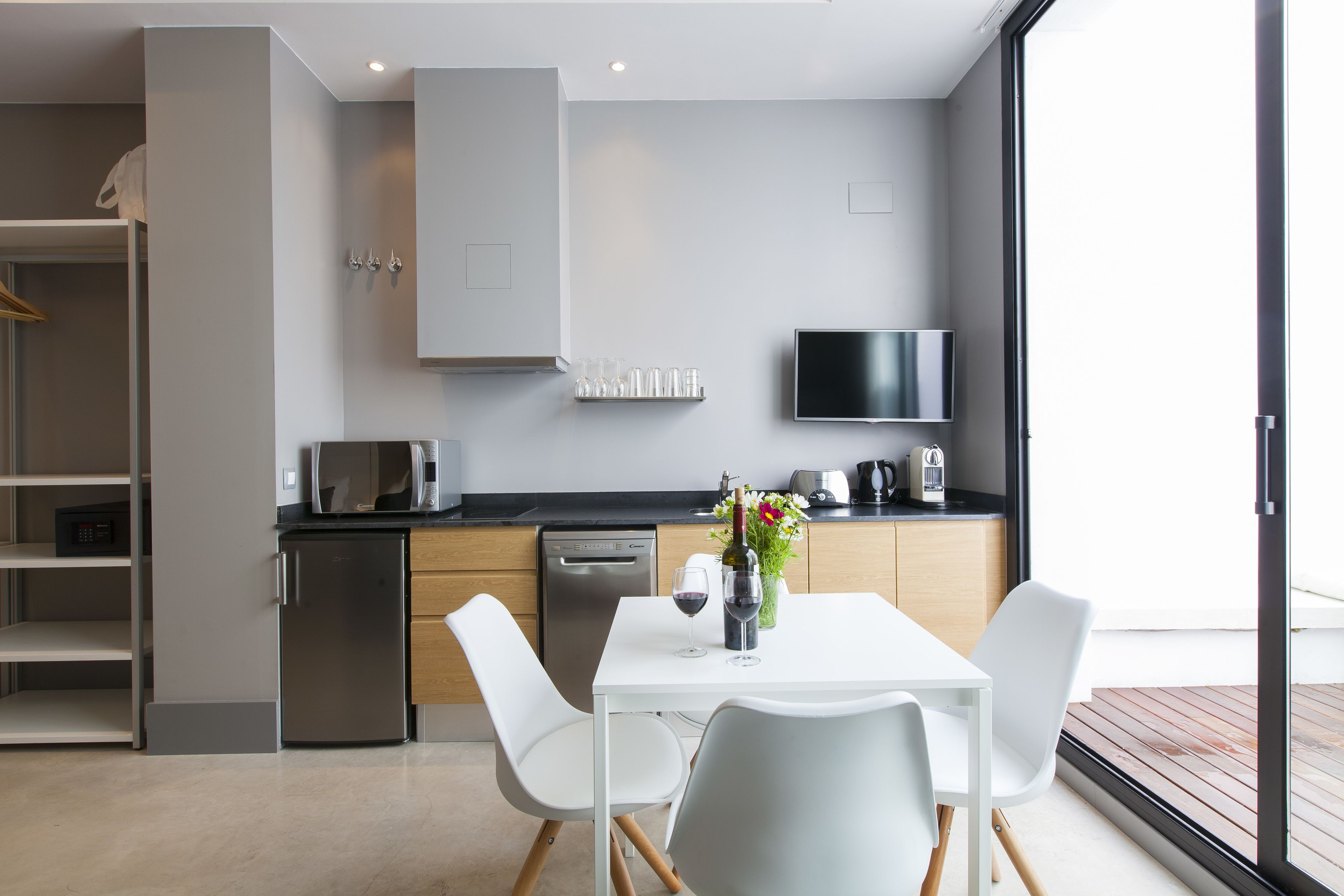 A modern kitchen with white cabinetry, a built-in microwave, a coffee maker, and a dining area with a white table and chairs.