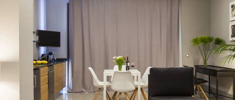 A modern living room with a dining area, a black sofa, a TV, and a plant.