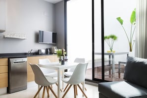 Une cuisine moderne équipée d’un lave-vaisselle, d’une table à manger avec des chaises blanches et d’une grande fenêtre donnant sur un balcon.