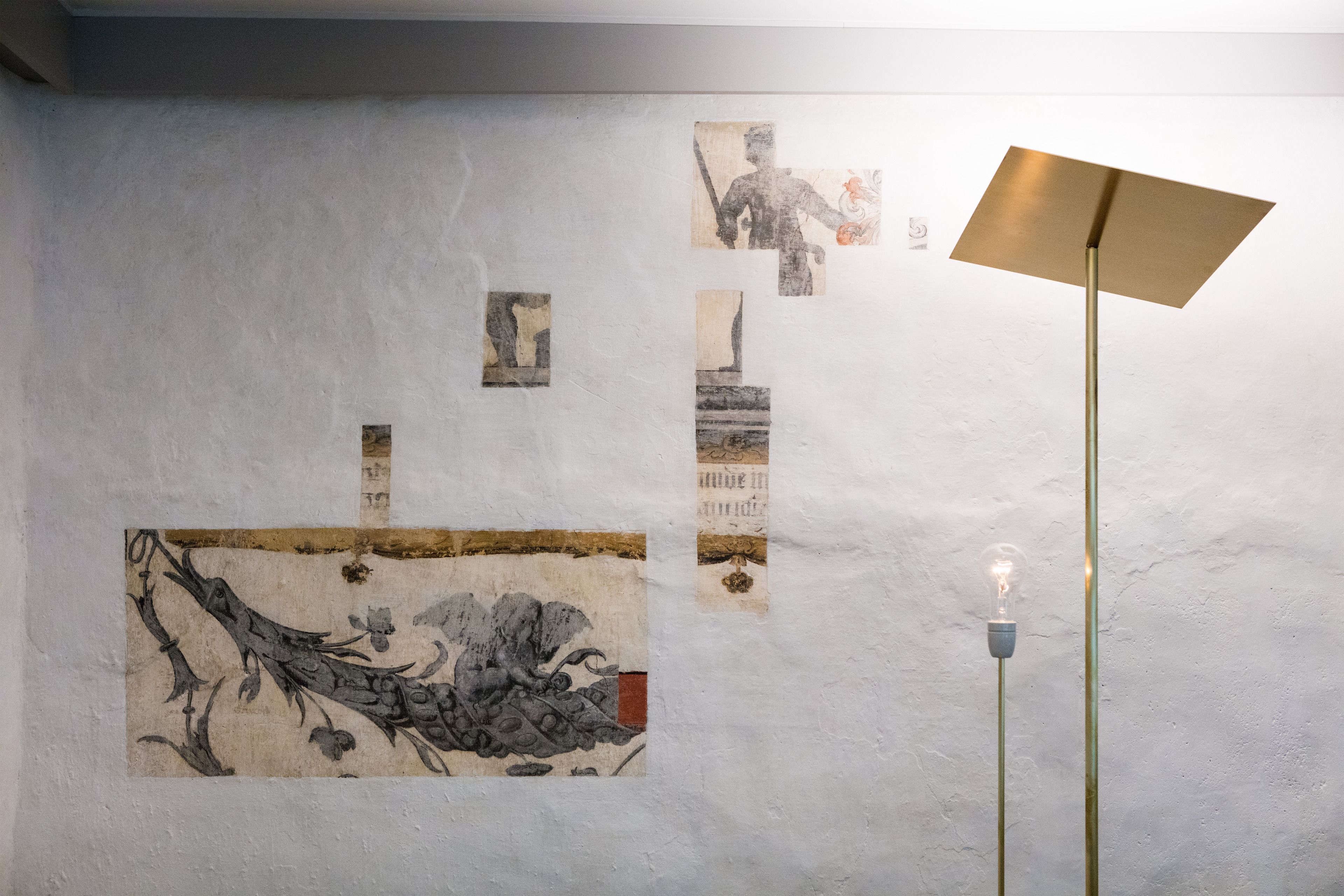 Eine Wand mit verschiedenen Kunstwerken und einer modernen Stehlampe.