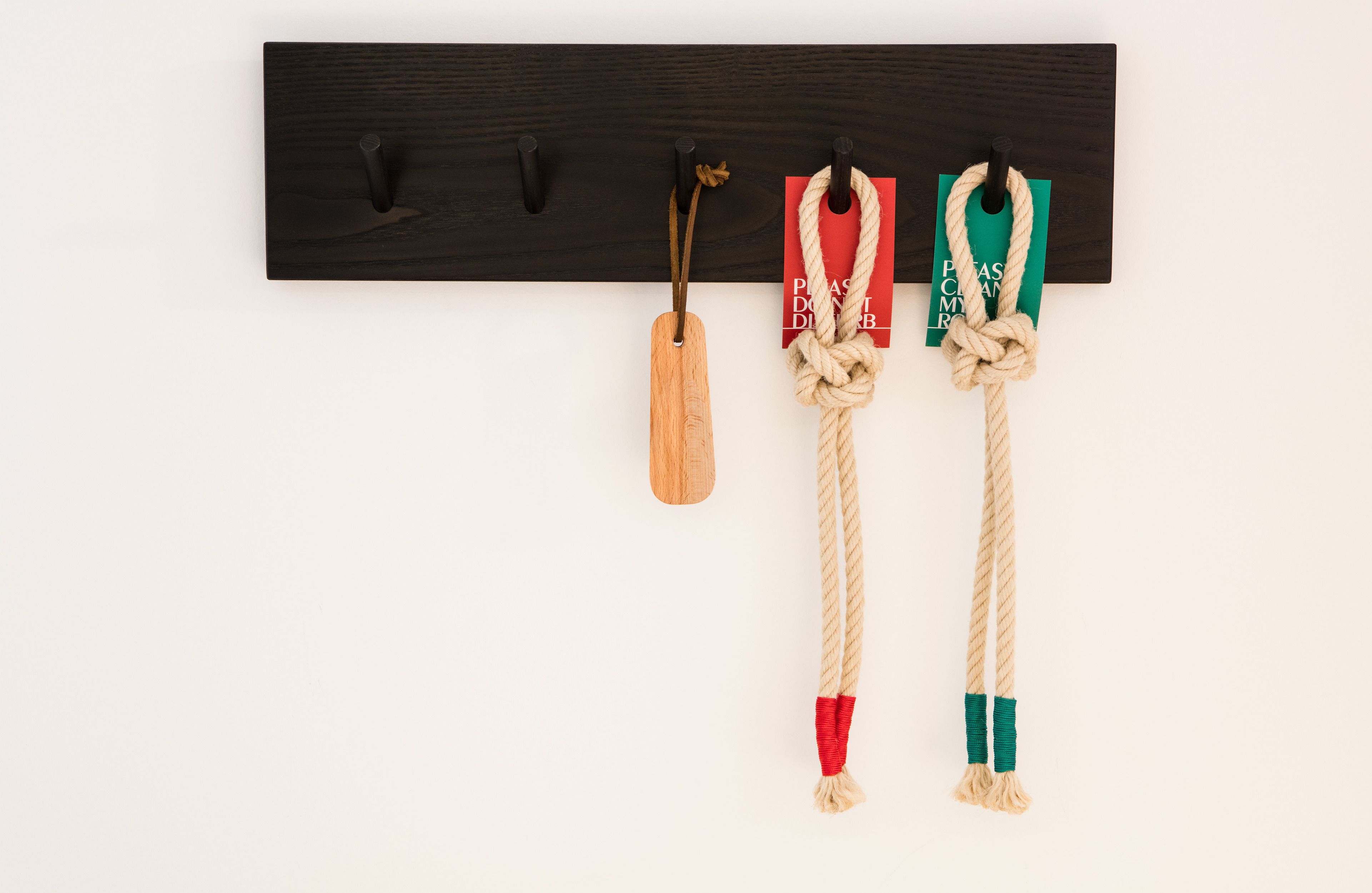 Un porte-manteau en bois doté de trois crochets, chacun servant à suspendre un objet différent : une étiquette en bois, une corde et une autre corde avec un nœud.