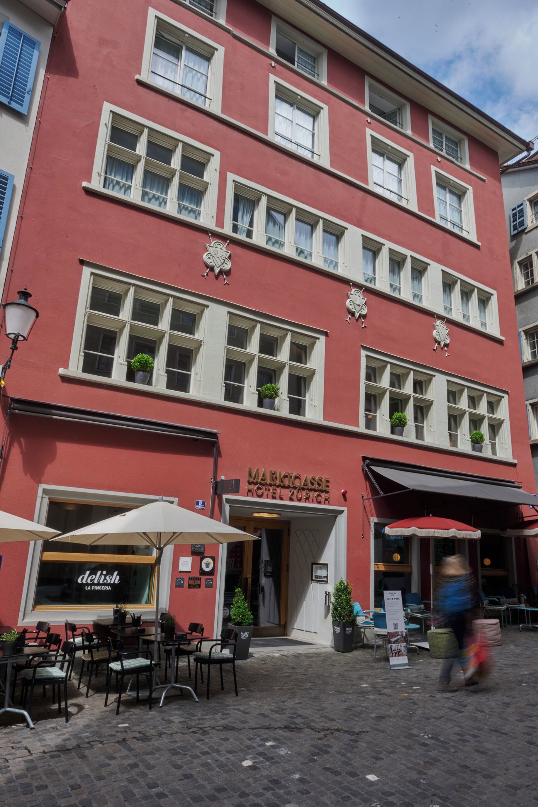 A red building with multiple windows, outdoor seating, and a sign for 'Marriott Hotel Zurich'.