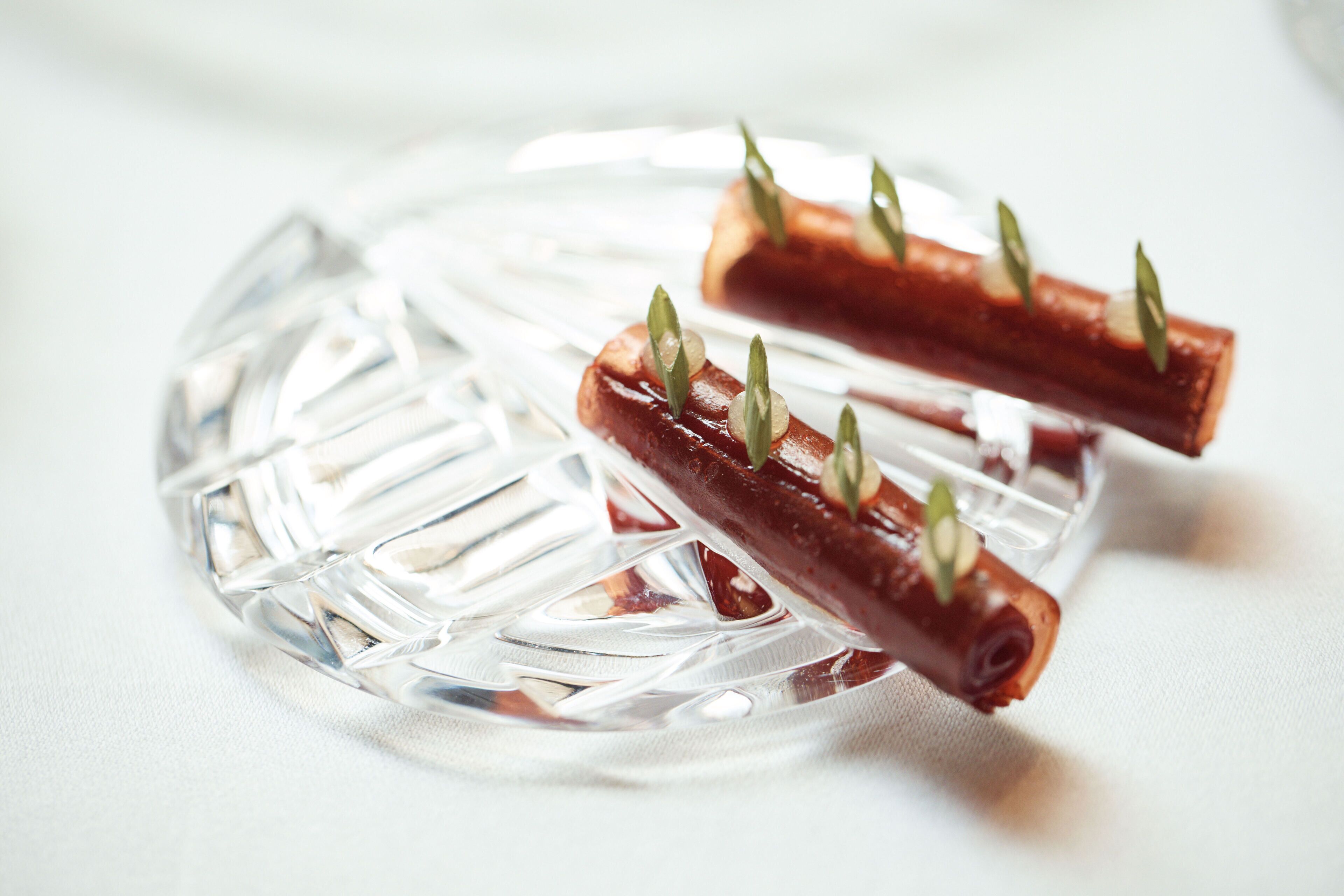 Une assiette en verre contenant deux brochettes de nourriture, chacune agrémentée d’une garniture verte.