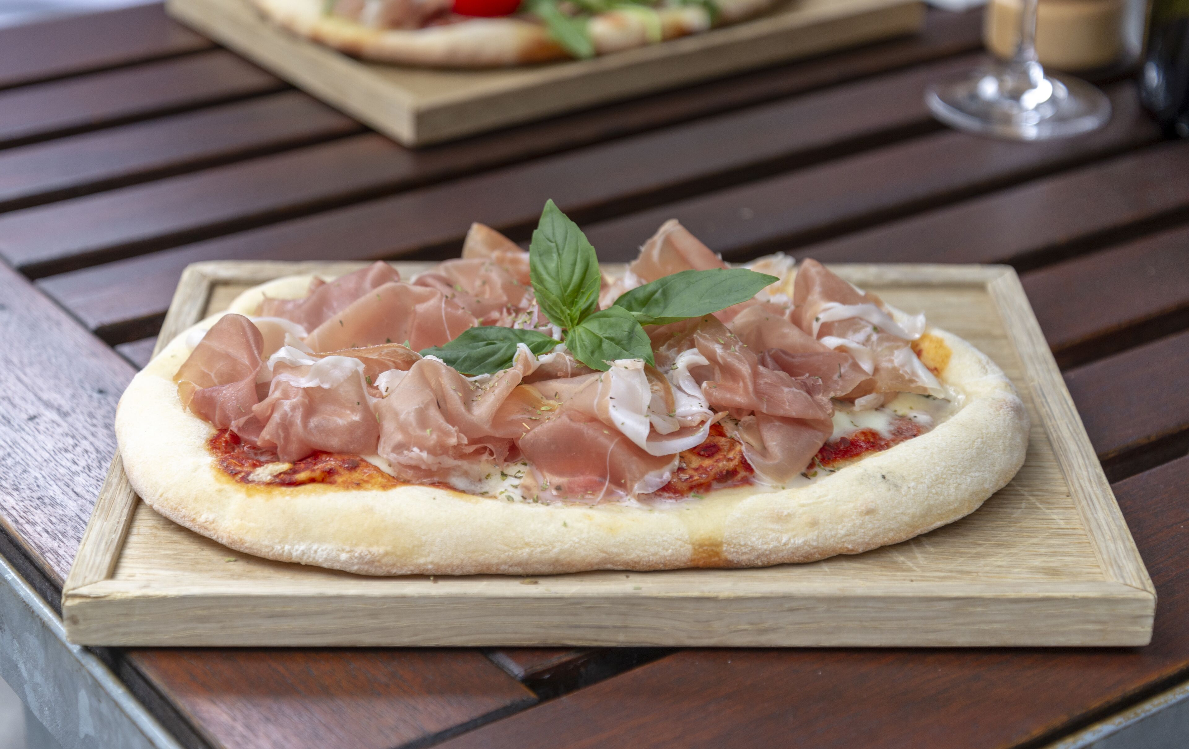 Eine Pizza auf einem Holzbrett mit Schinken und Basilikum auf einem Holztisch.