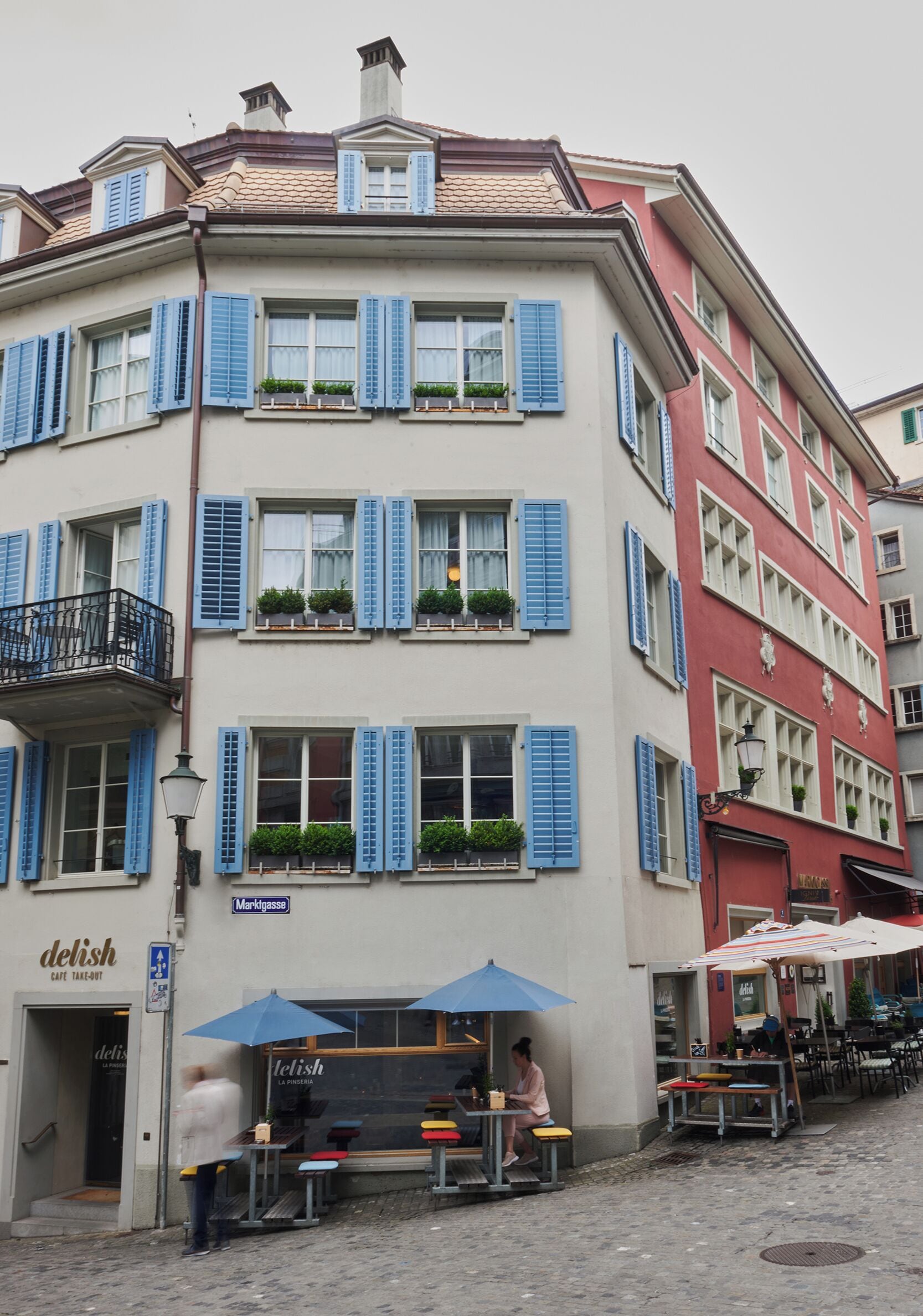 A building with multiple windows, some with shutters, and a café named 'delish' at the ground level.