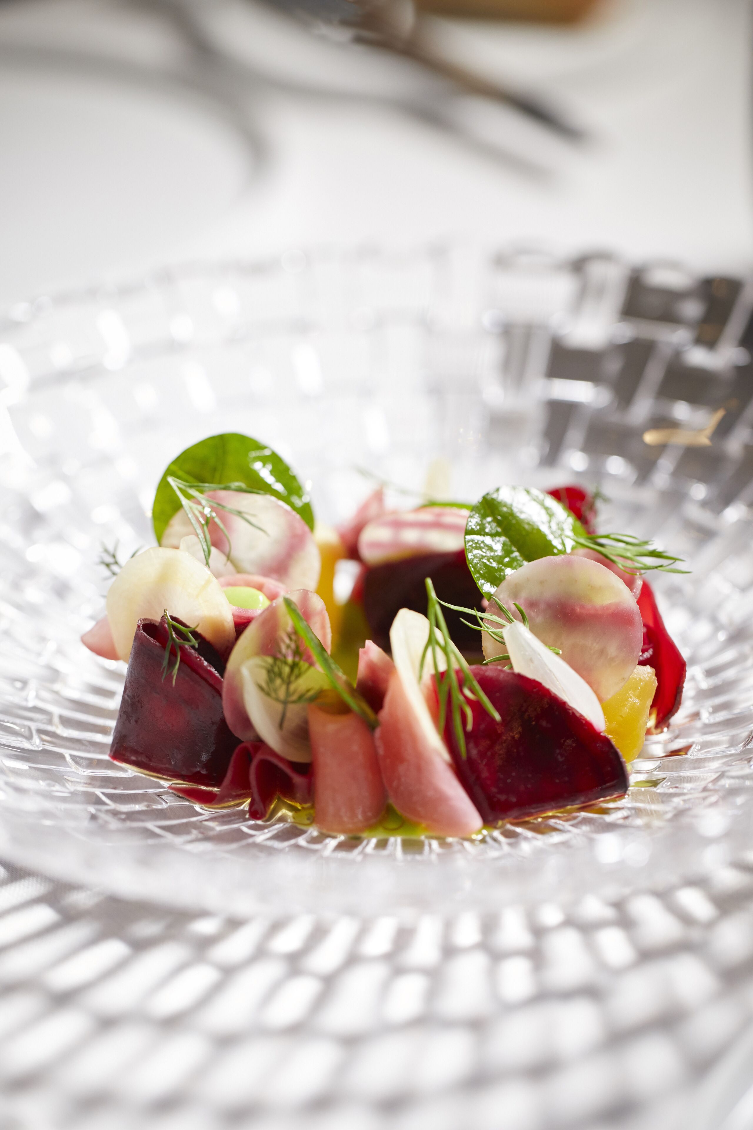 Un tazón de vidrio transparente con una ensalada colorida de diversos vegetales y hierbas.