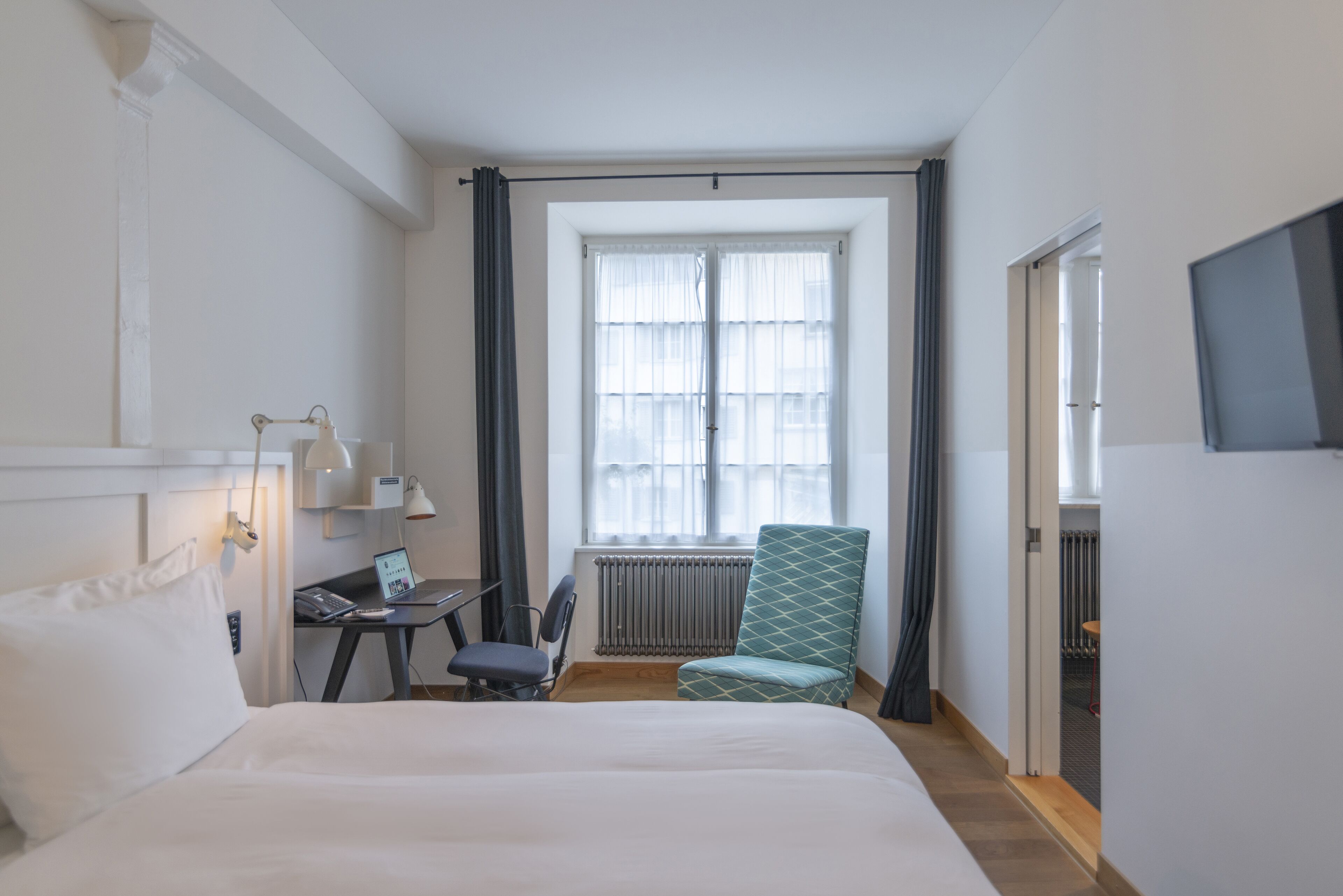 Ein Hotelzimmer mit Bett, Schreibtisch, Stuhl und einem Fenster mit Vorhängen.