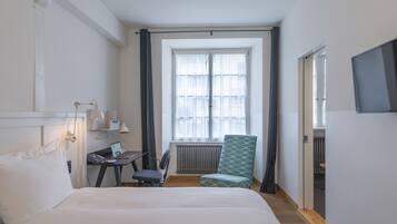 A hotel room with a bed, desk, chair, and a window with curtains.