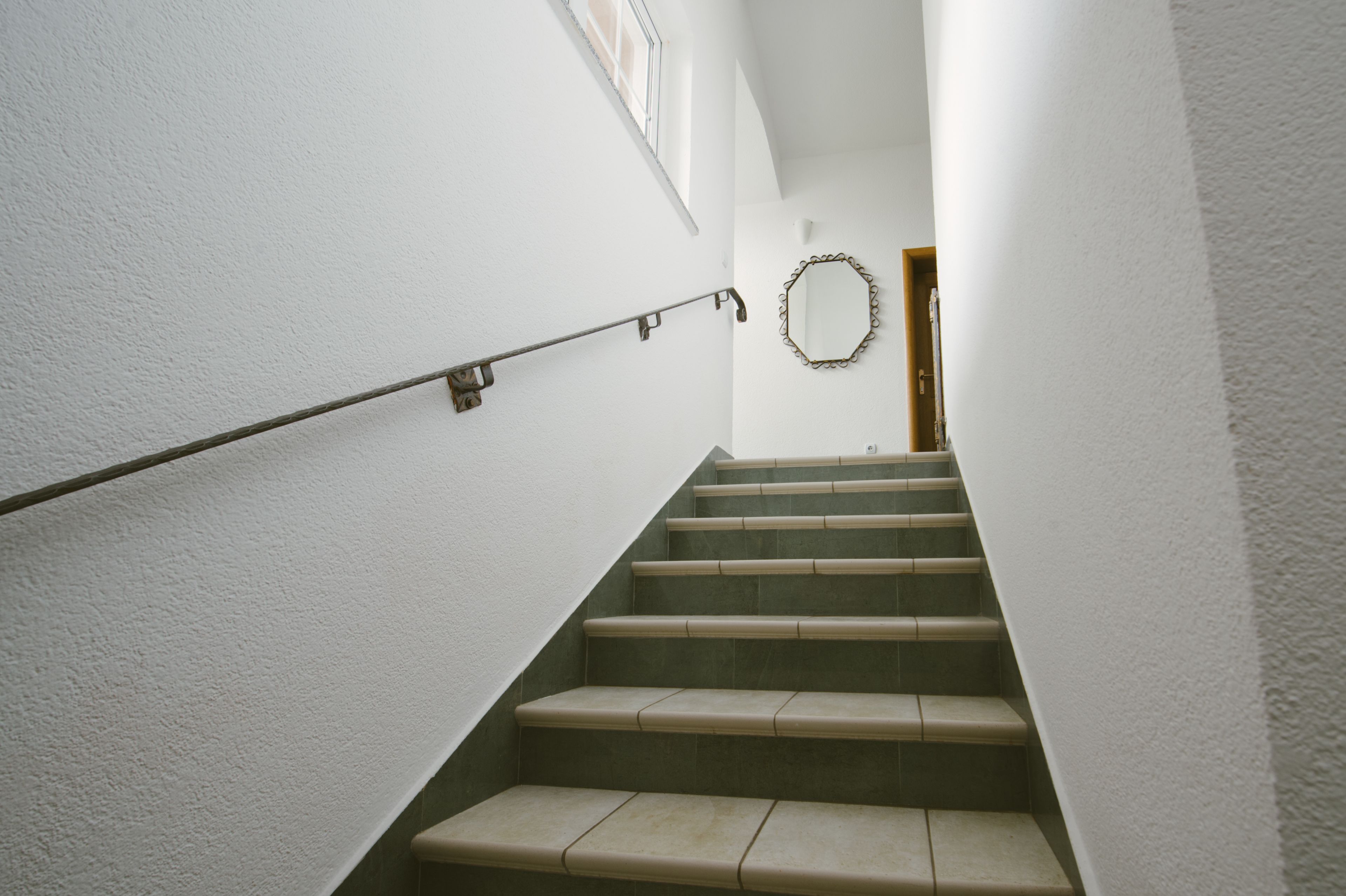 A staircase with a handrail, white walls, and a mirror on the wall.