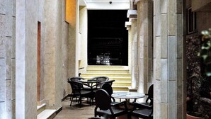 A corridor with tables and chairs, stone columns, and a view of a staircase leading to a darkened area. - Hotel Flowers (Citluk)