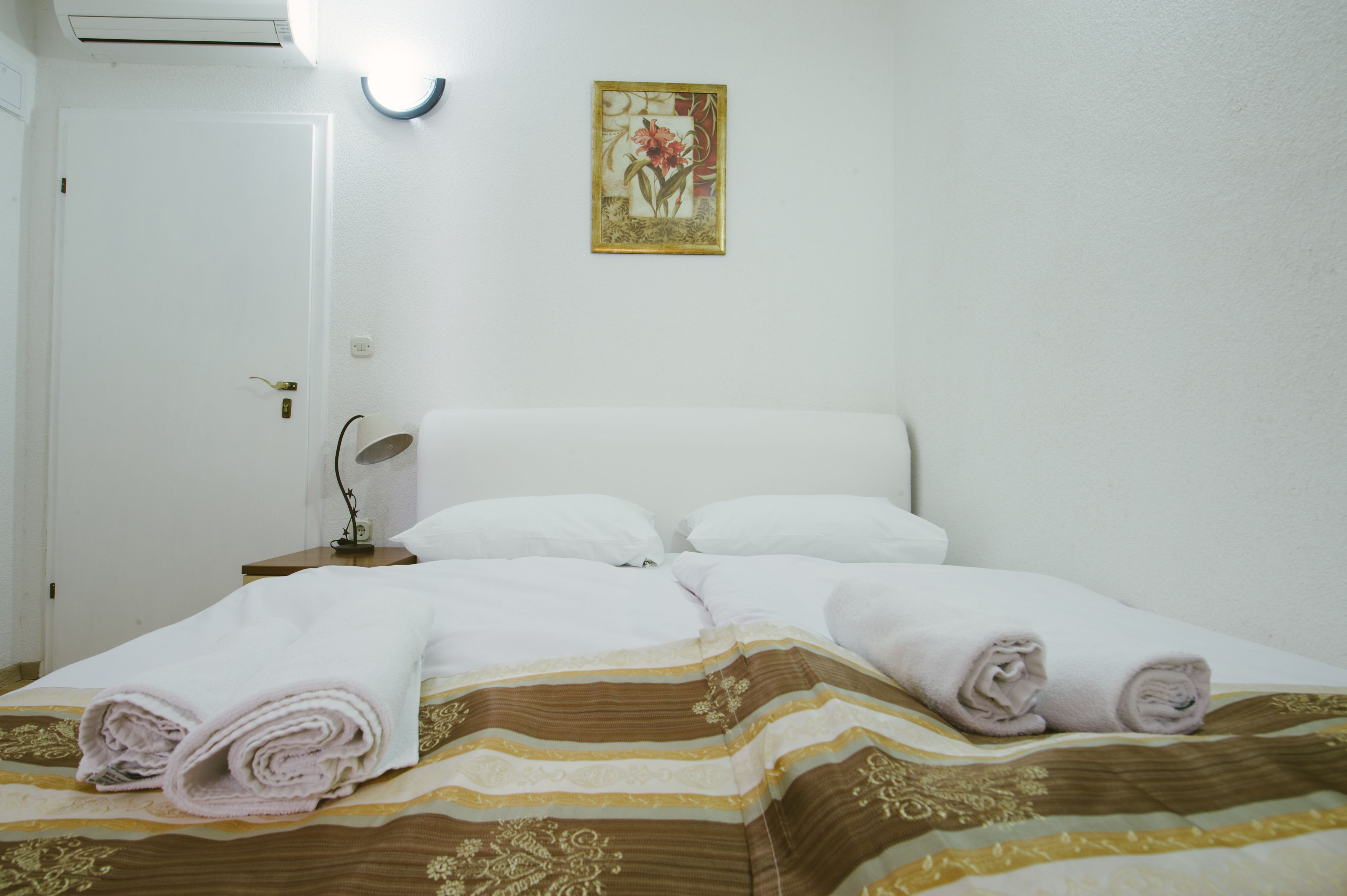 Ein ordentlich gemachtes Bett mit aufgerollten Handtüchern, einer Nachttischlampe und einem gerahmten Bild an der Wand.