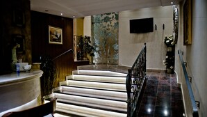 A staircase with a marble floor and a black railing, leading to a landing with a flat-screen TV mounted on the wall. - Hotel Flowers (Citluk)