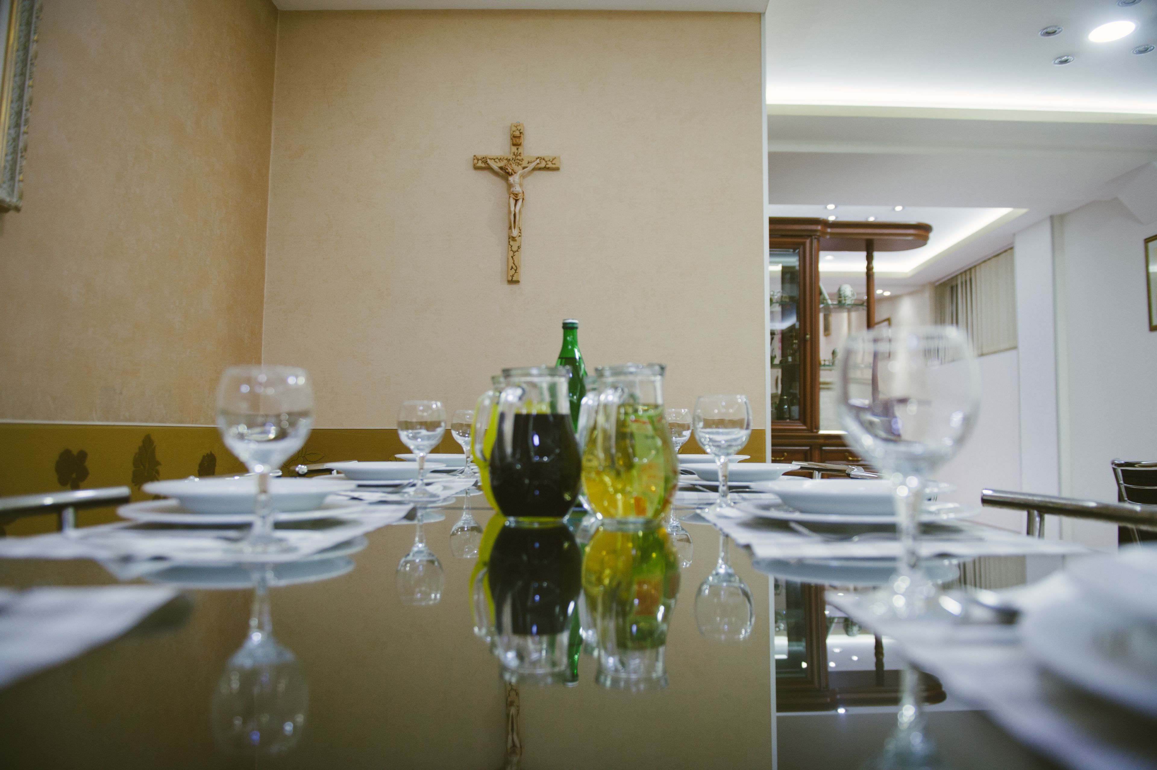 A dining table set with wine glasses and a cross on the wall.