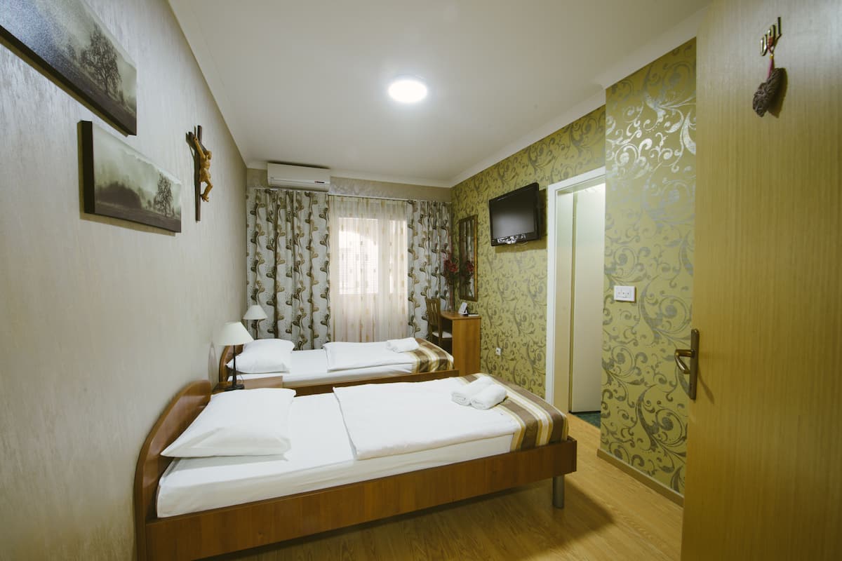 Hotellihuone, jossa on kaksi erillistä sänkyä, televisio, työpöytä ja tuoli.
