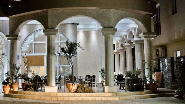 A hotel entrance with a covered outdoor seating area, columns, and large windows. - Hotel Flowers (Citluk)