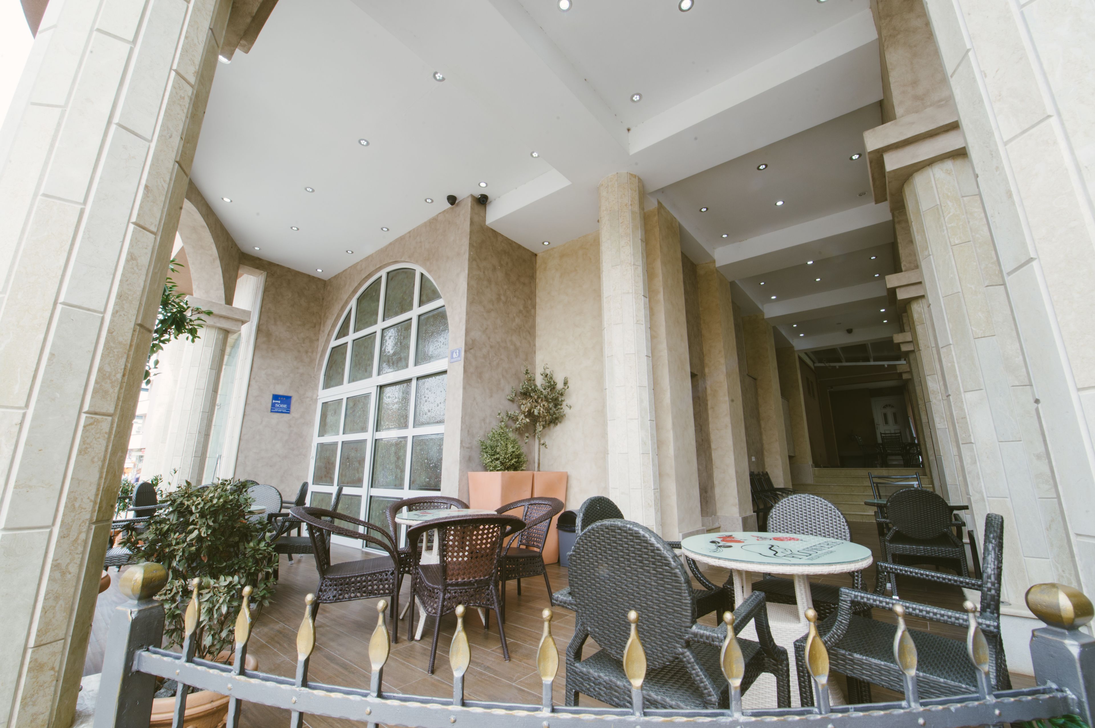 Ein Außenbereich eines Cafés mit Korbmöbeln, einem großen Rundbogenfenster und einem gefliesten Boden.