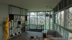 A modern living room with a large window, a sofa, a coffee table, a bookshelf, and a decorative sculpture. - Bonita Bay Concept Hotel by Xarm Hotels (Santa Marta)