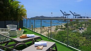 A balcony with outdoor seating, a view of the sea, and distant cranes. - Bonita Bay Concept Hotel by Xarm Hotels (Santa Marta)